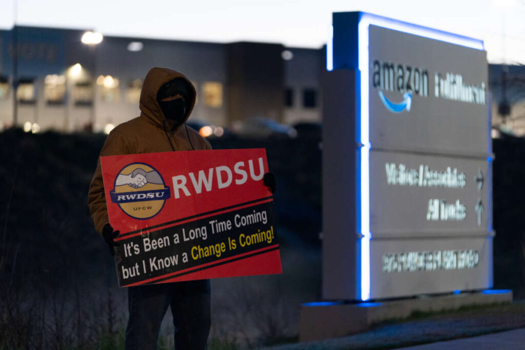Представитель профсоюза держит плакат у склада Amazon fulfillment в центре громкой акции по объединению профсоюзов 29 марта 2021 года в Бессемере, штат Алабама./ Фото: ELIJAH NOUVELAGE / GETTY IMAGES